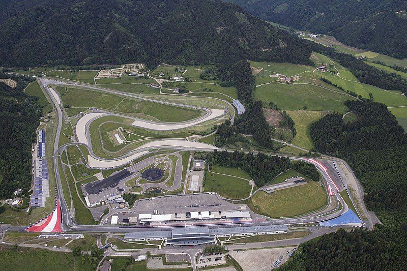 Luchtfoto van het Red Bull Ring-circuit in Oostenrijk, omgeven door groene heuvels en bossen. Het circuit heeft verschillende bochten en rechte stukken.