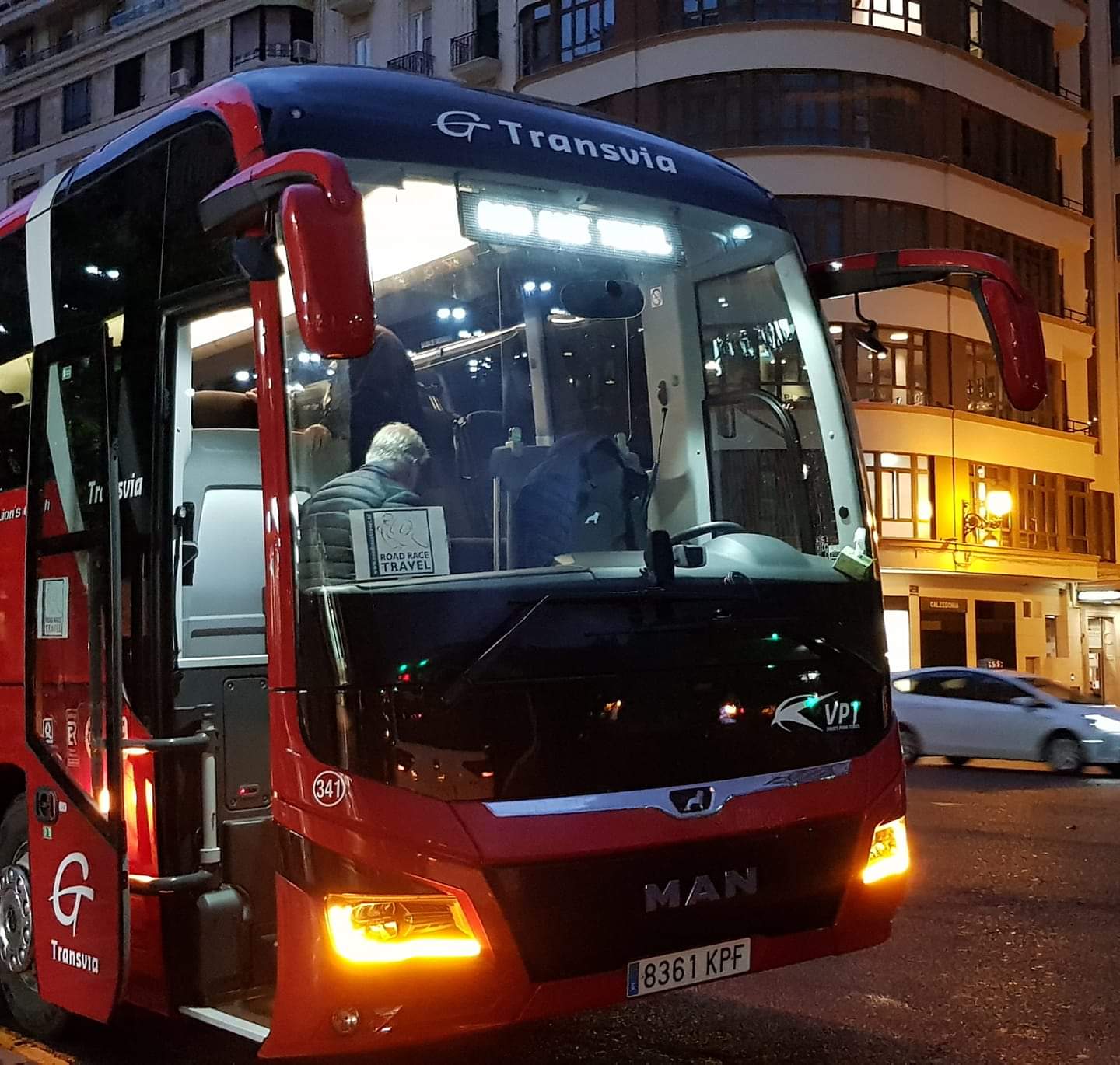 Een rood-zwarte Transvía-bus geparkeerd op een nachtelijke straat in de stad. De chauffeur is zichtbaar.