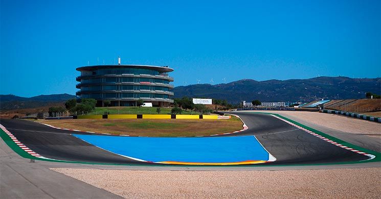 Racebaan met een opvallend rond gebouw op de achtergrond onder een helderblauwe lucht. De baan is voorzien van kleurrijke markeringen.