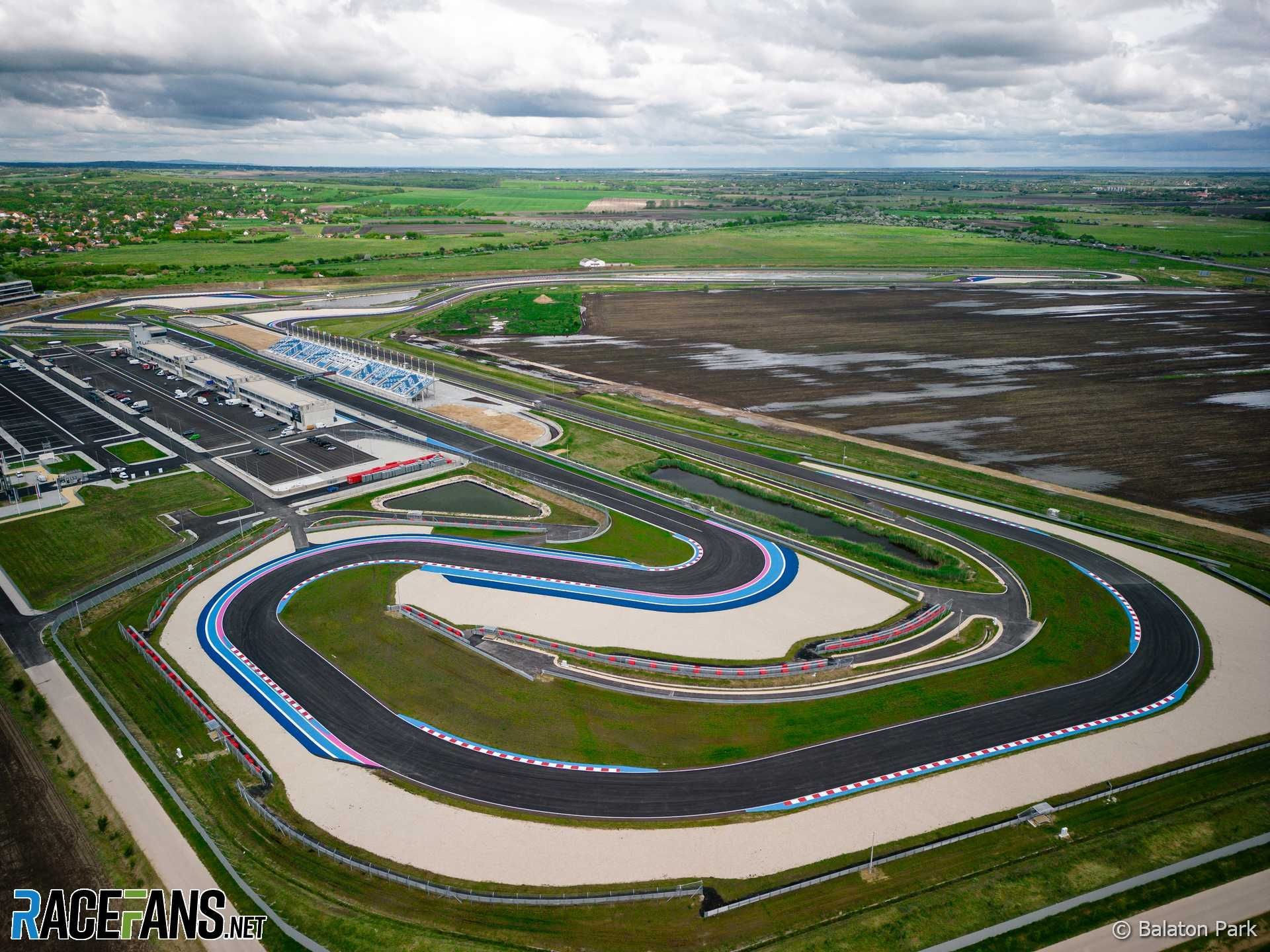 Luchtfoto van het Hungaroring-racecircuit met verschillende bochten, een pitstraat en het omliggende groene landschap onder een bewolkte hemel.