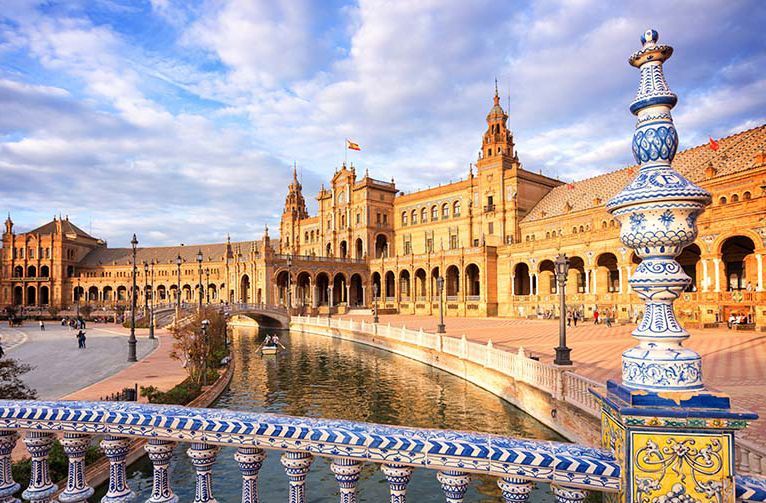 Een zonnig uitzicht op de Plaza de España in Sevilla, Spanje, met een kanaal, sierlijke architectuur en blauwe en witte keramische details.