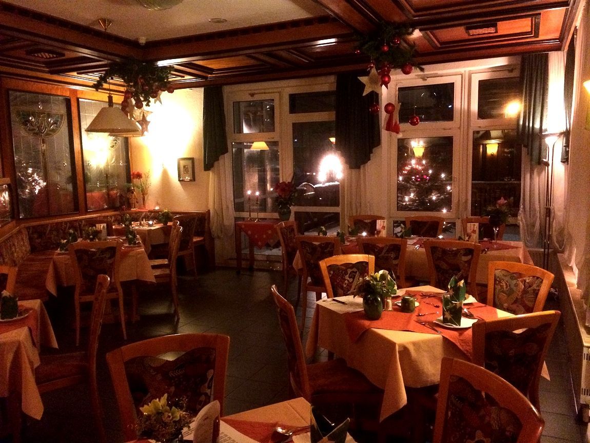 Interieur van een warm verlicht restaurant met gedekte tafels voor diners. Donkere houten lambrisering en rode accenten zorgen voor een gezellige sfeer.