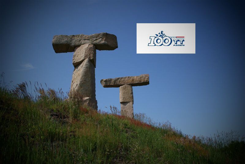 Stenen bouwwerken op een met gras begroeide heuvel onder een blauwe lucht, met een