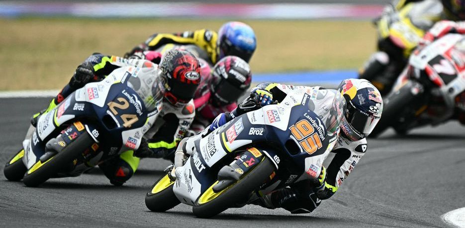 Motorcoureurs leunen in een bocht op een circuit. Close-up met de kopman in wit en blauw.