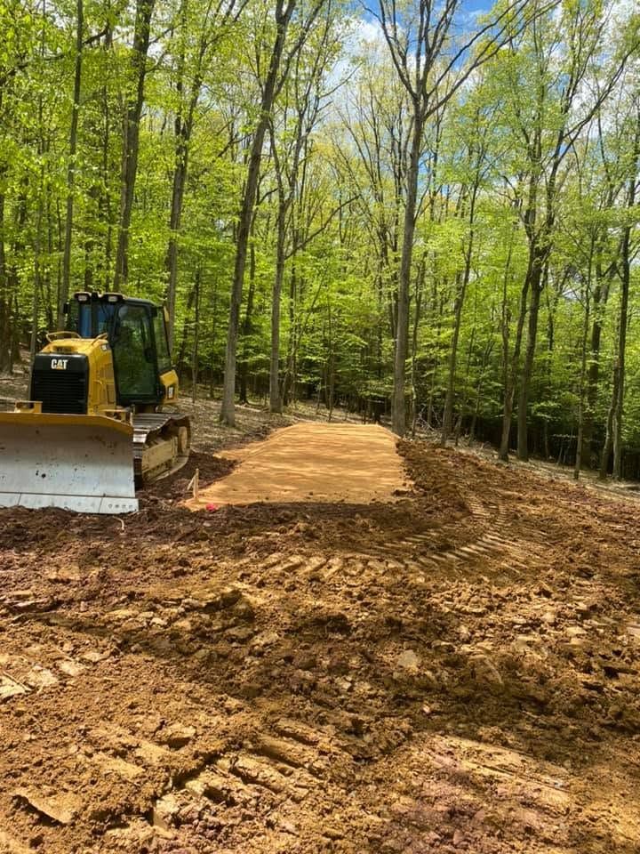 Bulldozer grading a dirt path in a wooded forest clearing under green trees