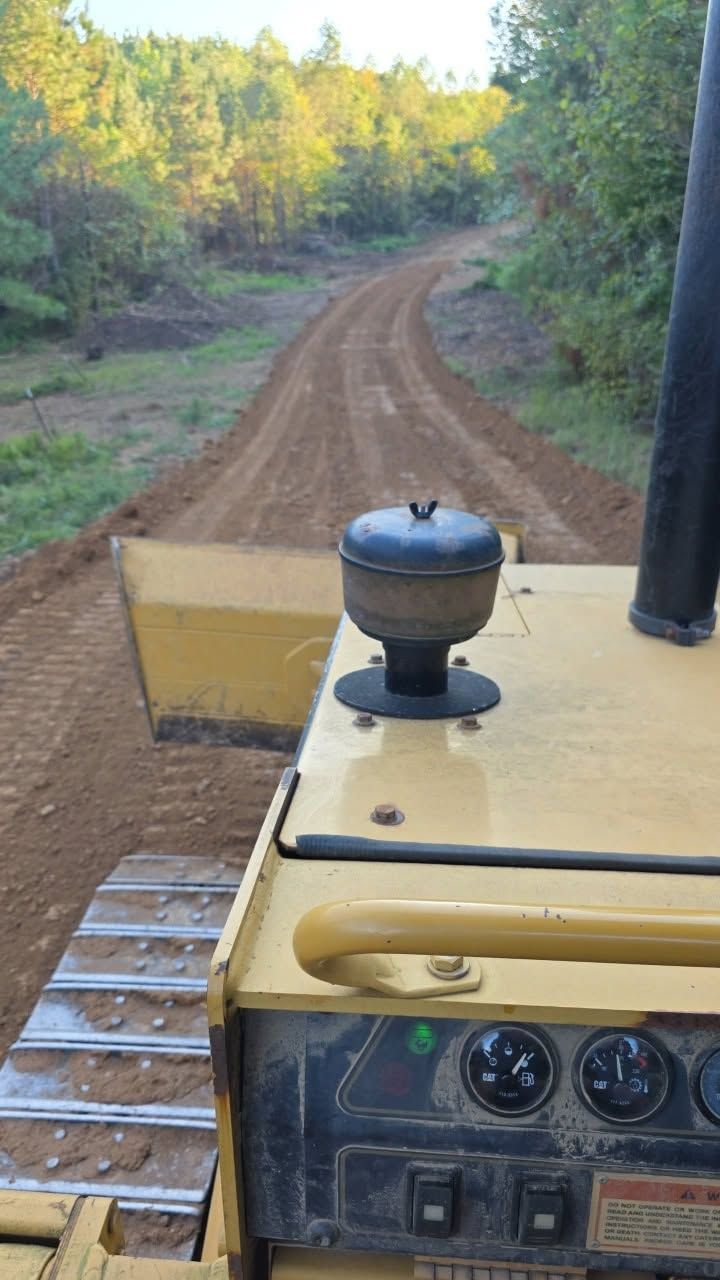 View from a construction vehicle driving on a dirt road through a wooded area.