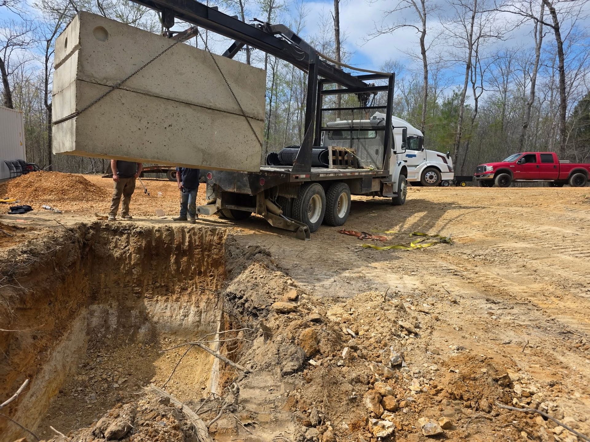 Dump truck unloading a large concrete tank beside a deep excavation on a muddy construction site