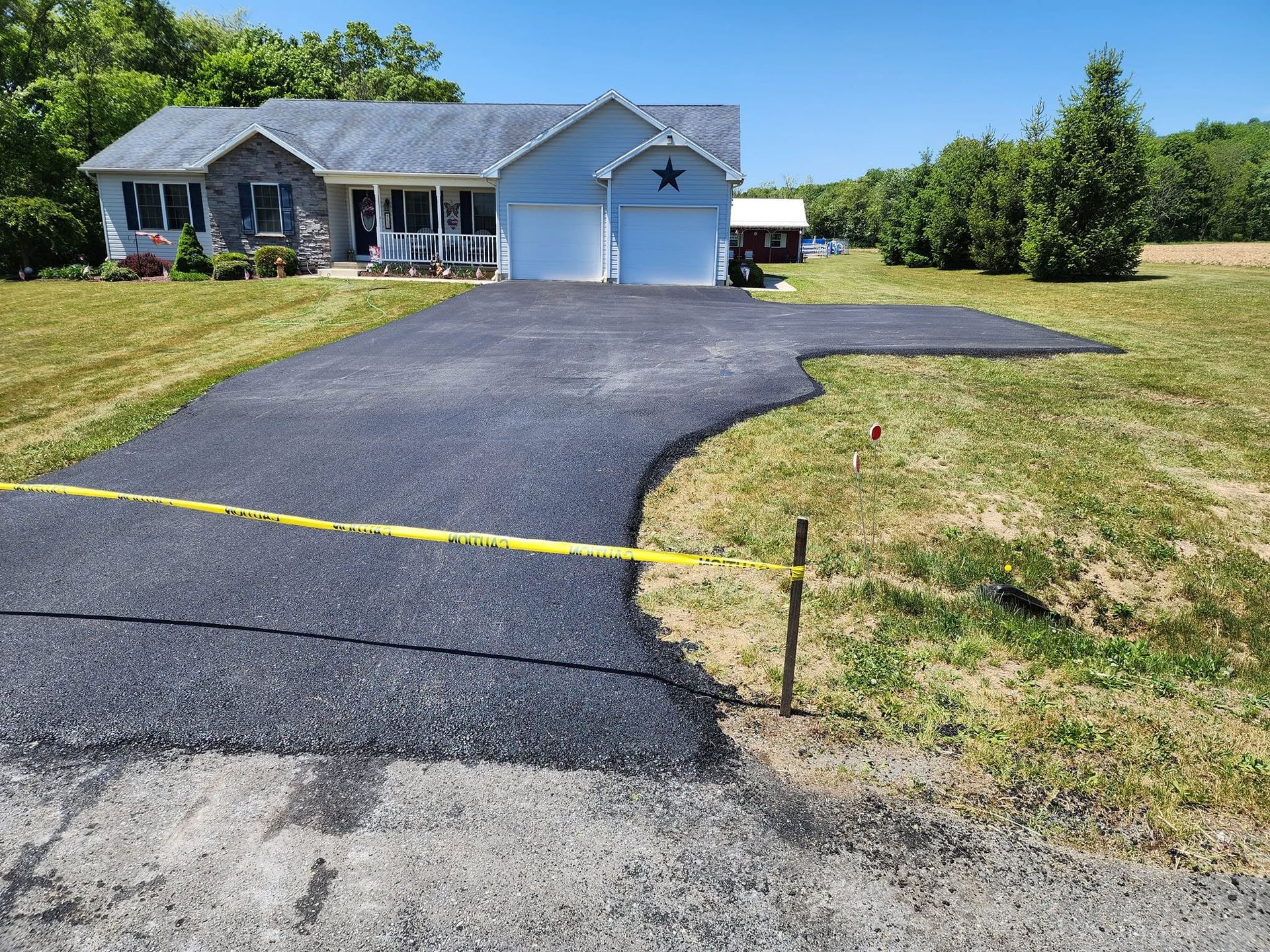 Suburban house with a freshly paved black driveway and yellow caution tape in the foreground