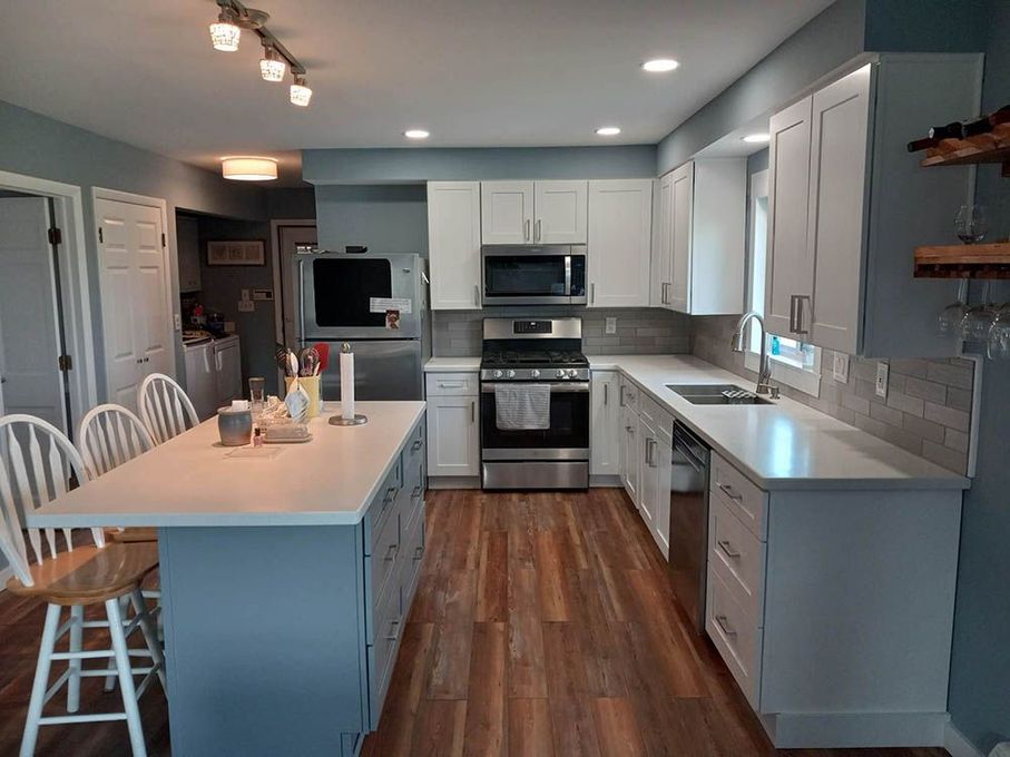 A kitchen with white cabinets , stainless steel appliances , hardwood floors and a large island.