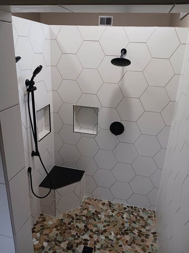 A shower with white tiles and a black shower head.