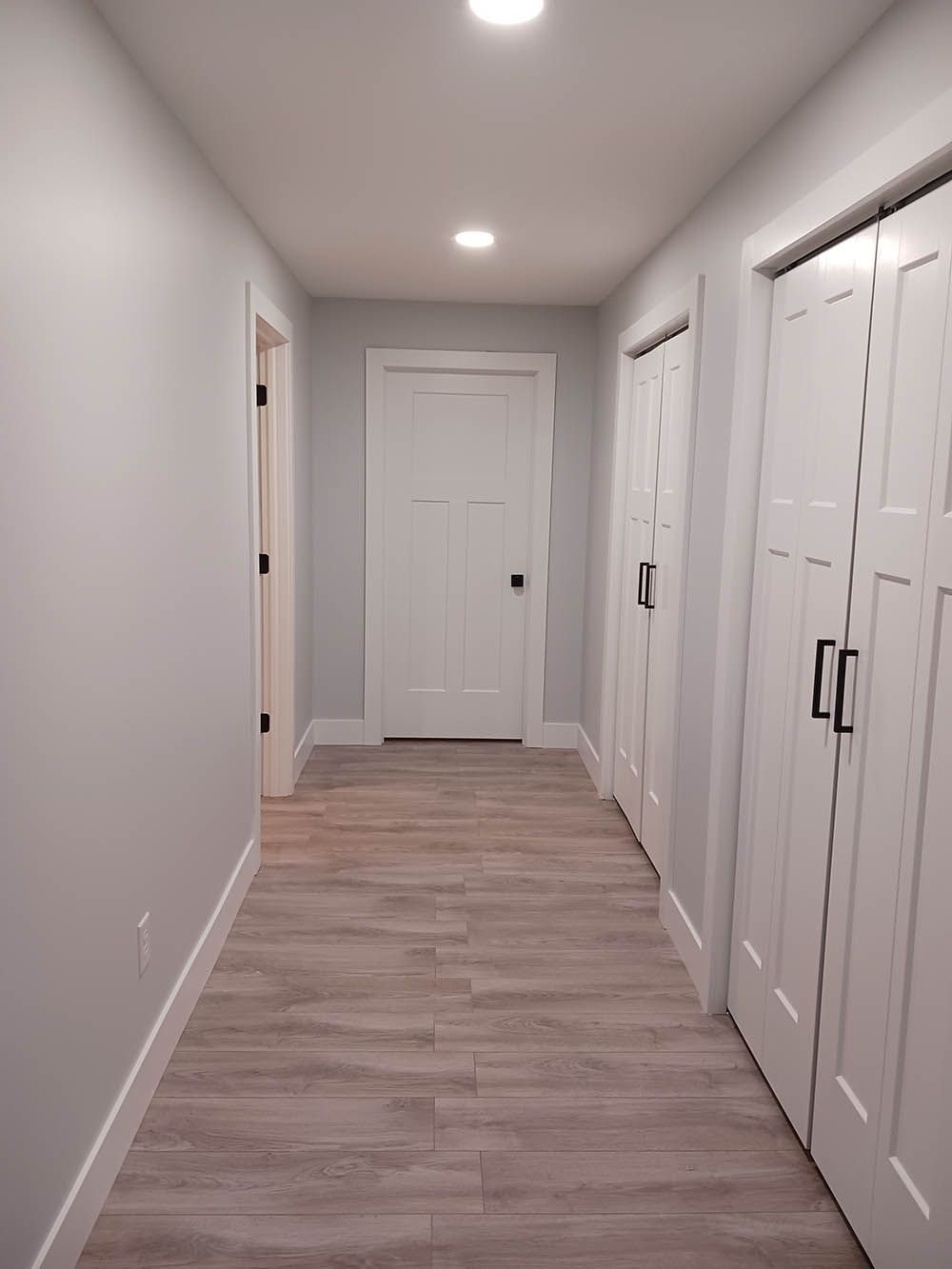 A long hallway with wooden floors and white cabinets leading to a door.