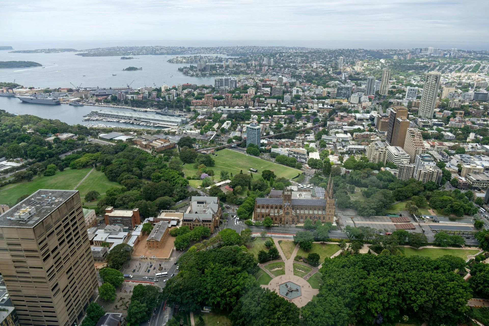 Aerial view of a coastal city with harbor, dense buildings, and green parkland under cloudy skies