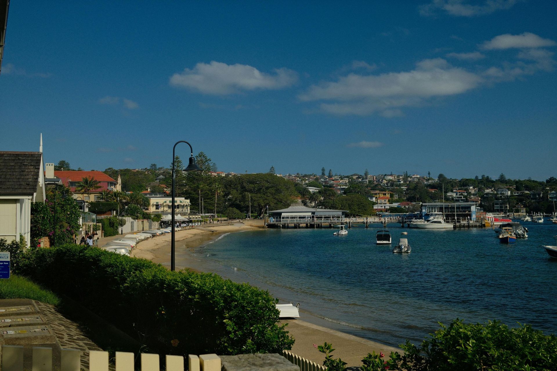 Harbor shoreline with boats, sandy beach, and buildings under a blue sky