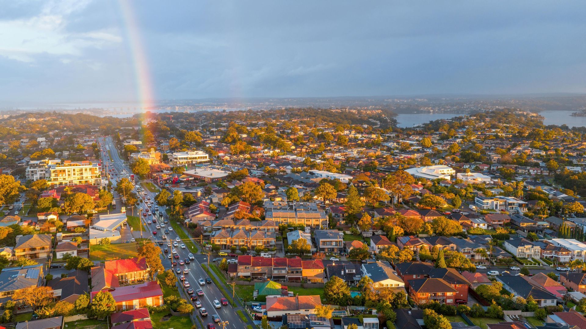 Aerial view of a colorful coastal town at sunset, with a rainbow and water in the distance.