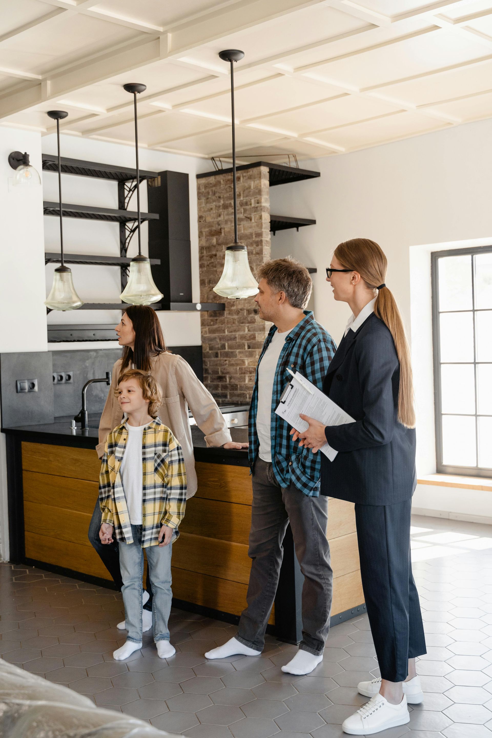 Three people and a child stand in a bright loft kitchen, looking at the room during a tour.