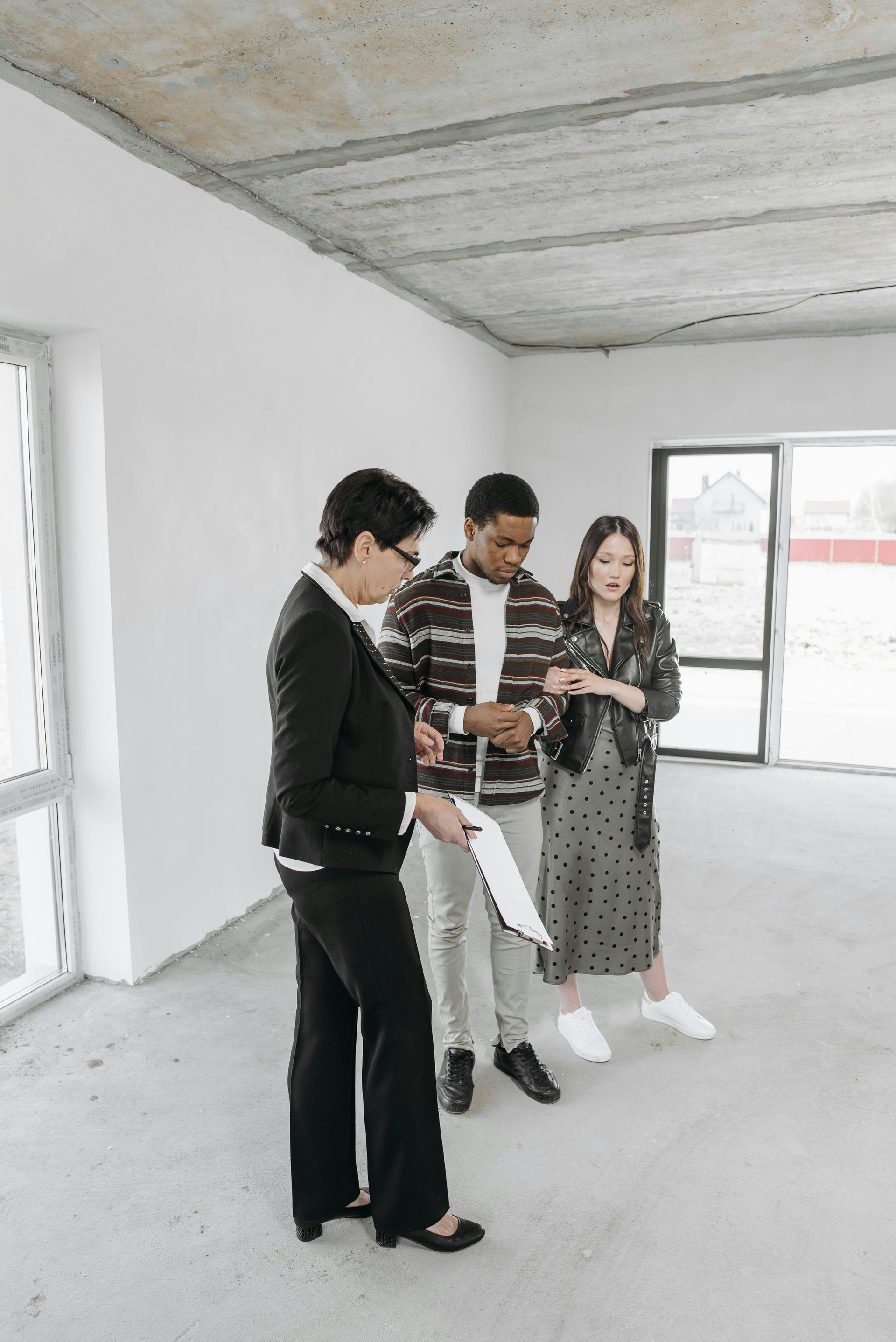Three people in a bare unfinished room stand together looking at a phone.