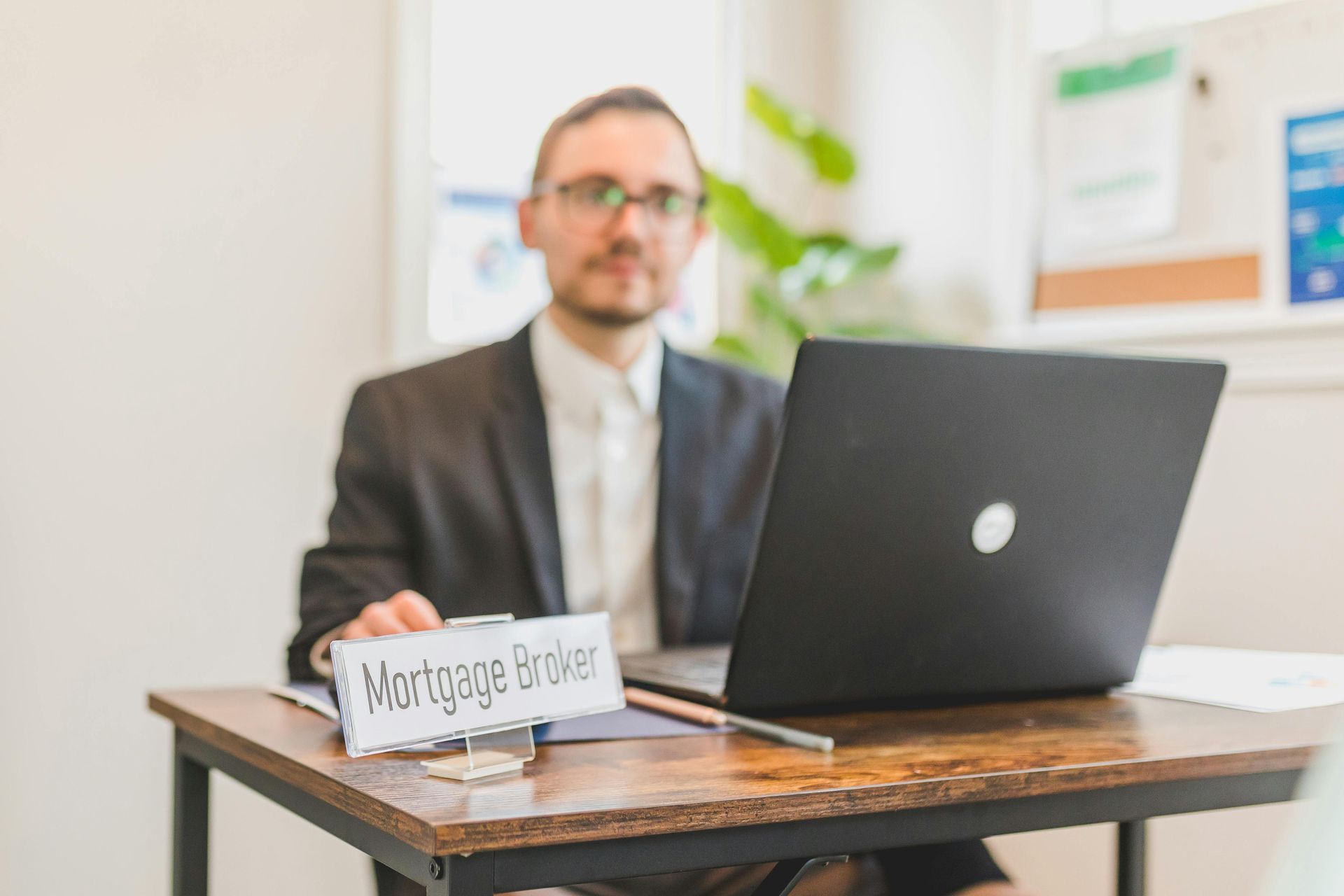 Man in a suit sitting at a desk with a laptop and a small “Work from home” sign