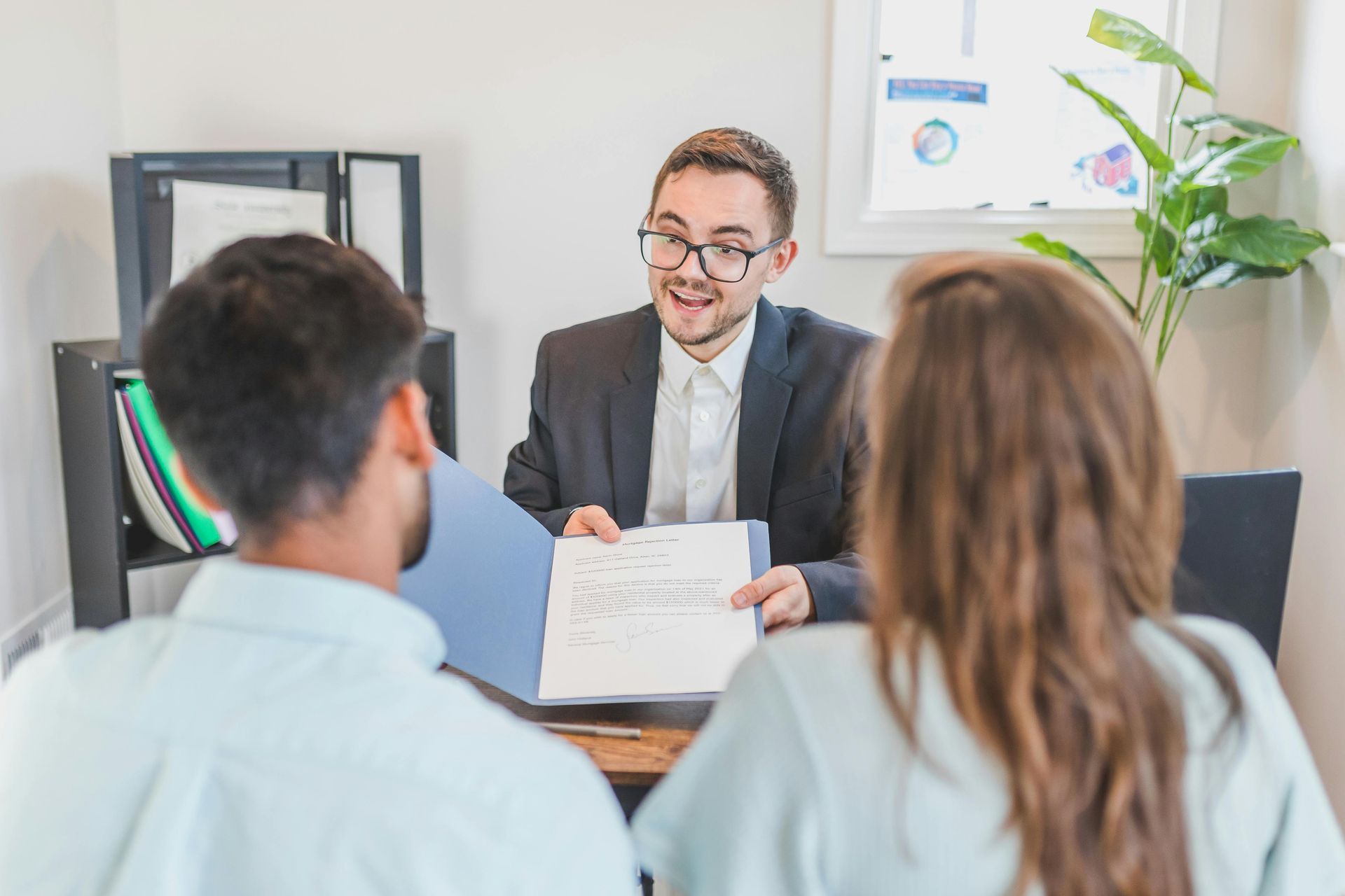 Meeting in an office: a man presenting papers to two seated clients across a desk