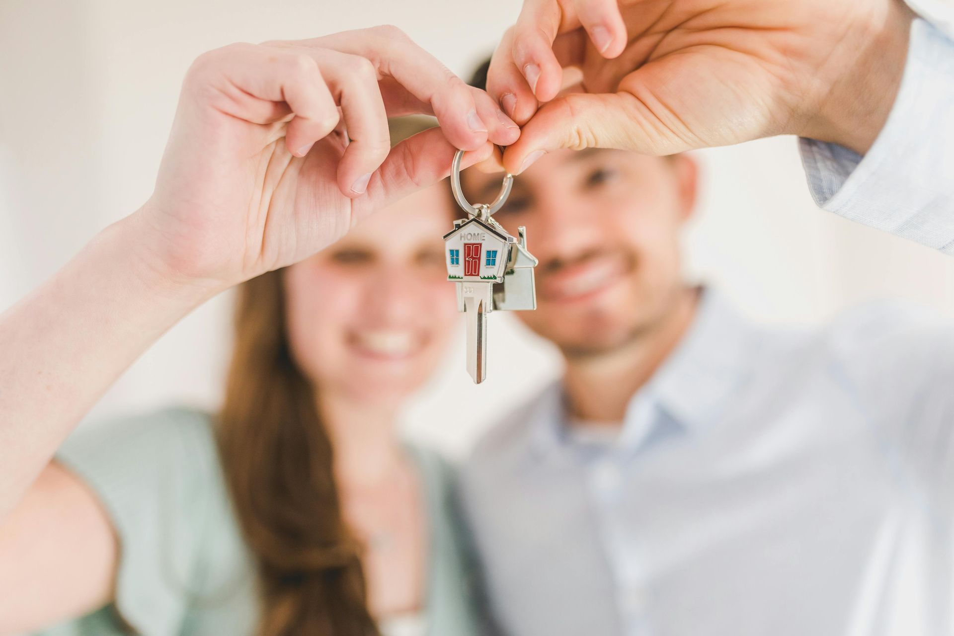 Hands holding up a house key in front of a smiling couple