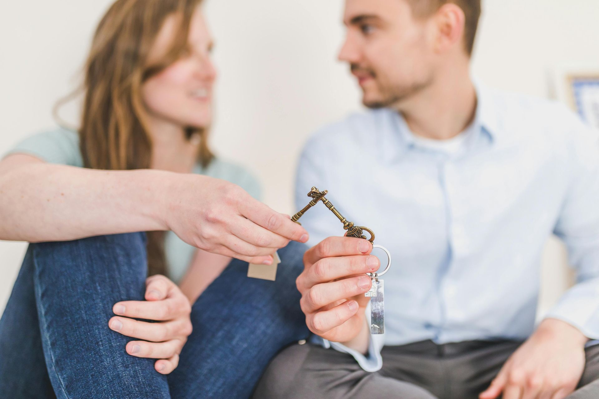 Woman handing a key to a man in a bright room, suggesting a home or car transfer