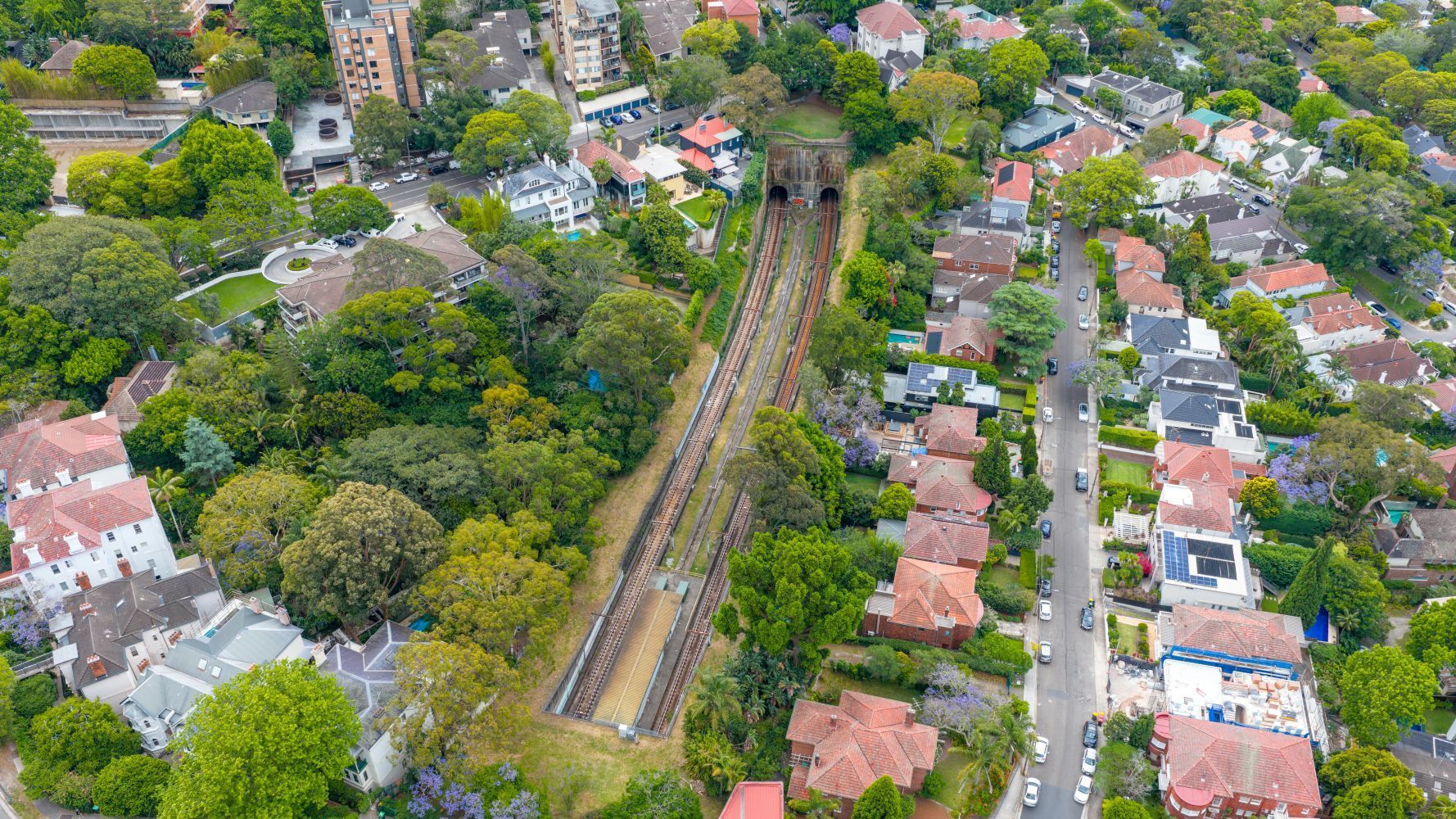 Aerial view of railway tracks cutting through a green residential neighborhood with houses on both sides