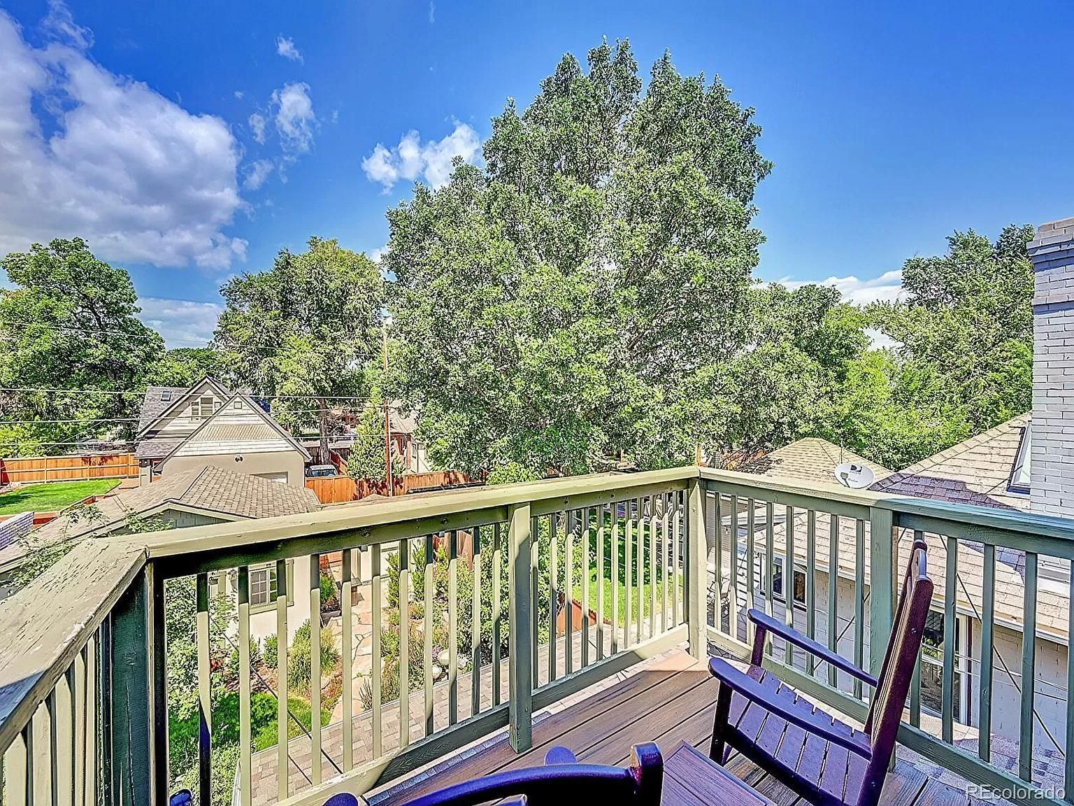 A balcony with a chair and a view of trees and a house.