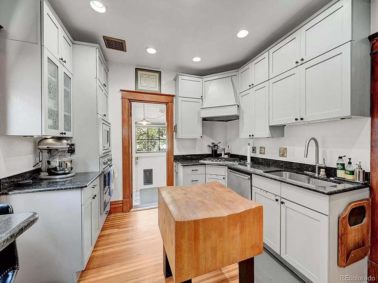 A kitchen with white cabinets , granite counter tops , and a wooden island.