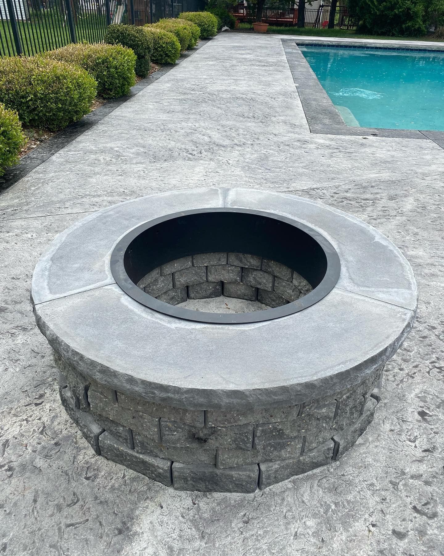 A fire pit is sitting on a patio next to a pool.