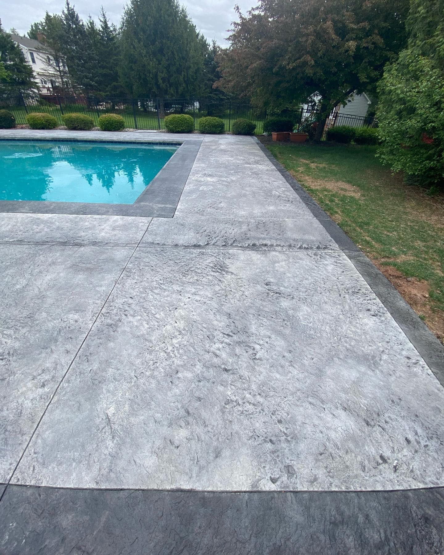 A concrete walkway leading to a swimming pool in a backyard.
