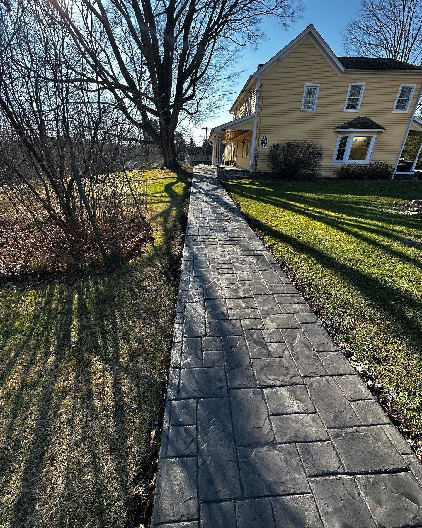 A brick walkway leading to a large yellow house.