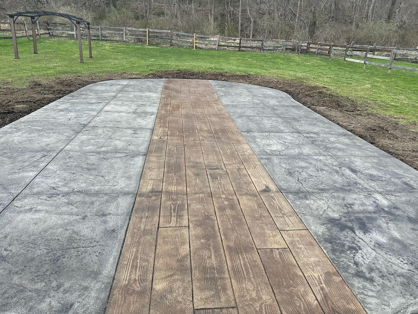 A concrete walkway with a wooden border and a fence in the background.