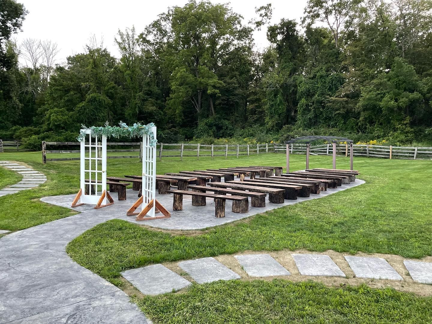 A row of wooden benches are lined up in a field for a wedding ceremony.