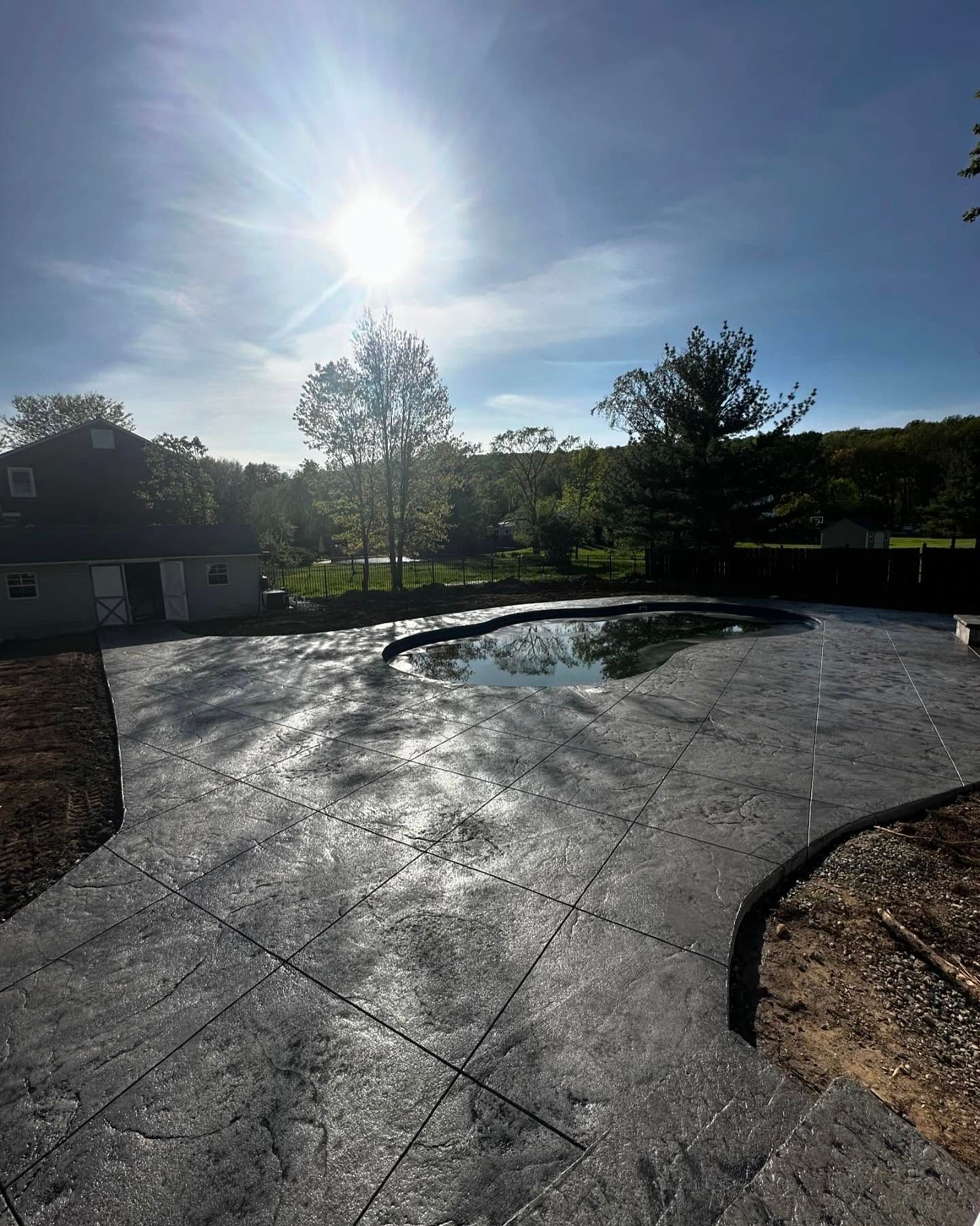A concrete patio with a pool in the background and a house in the background.