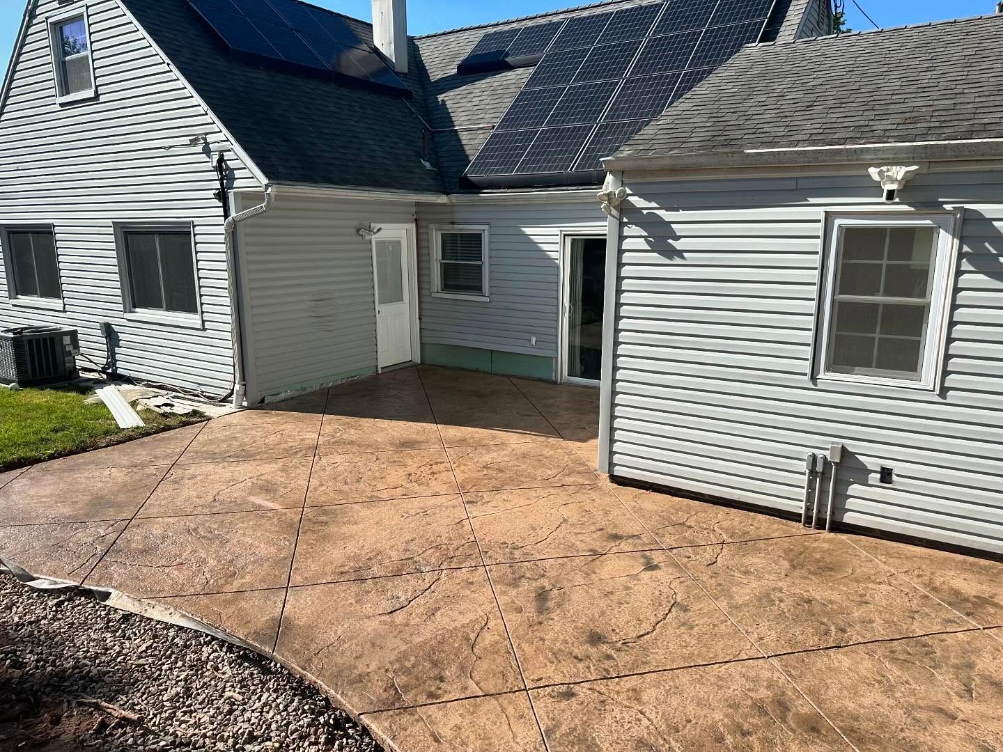 A white house with a patio in front of it and a solar panel on the roof.