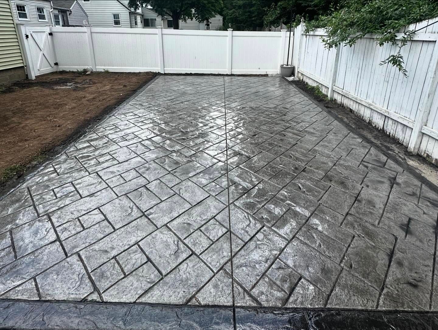 A concrete driveway with a white fence in the background.
