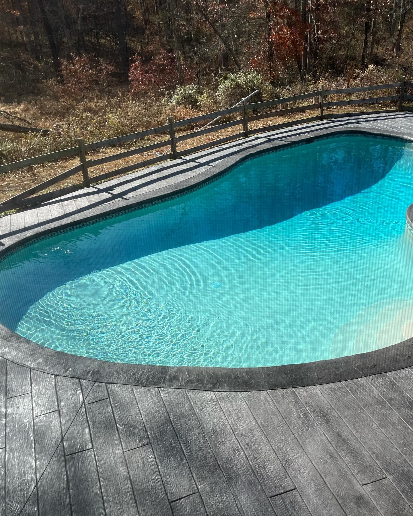 A large swimming pool surrounded by trees and a wooden deck.