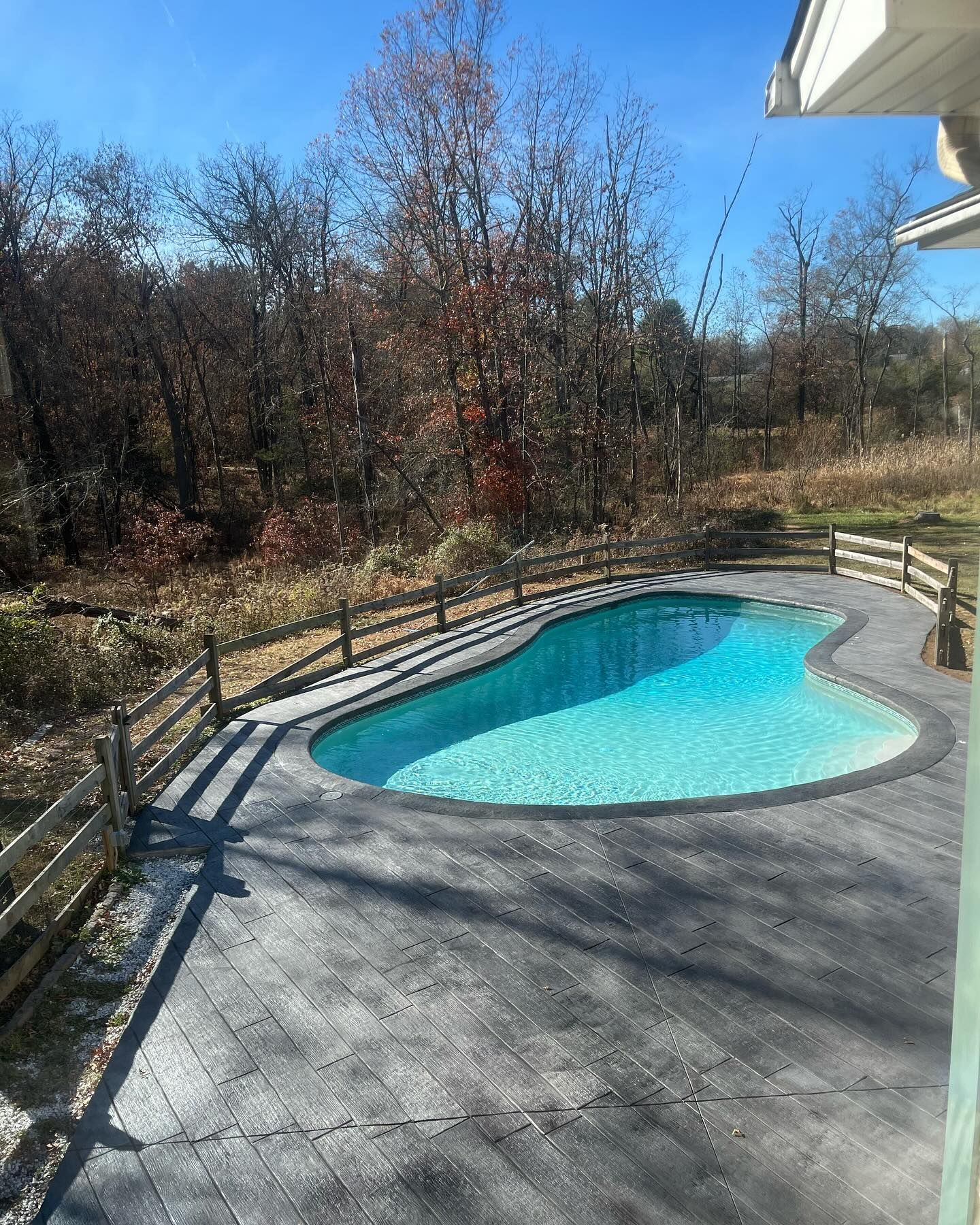 A large swimming pool is surrounded by trees and a fence.