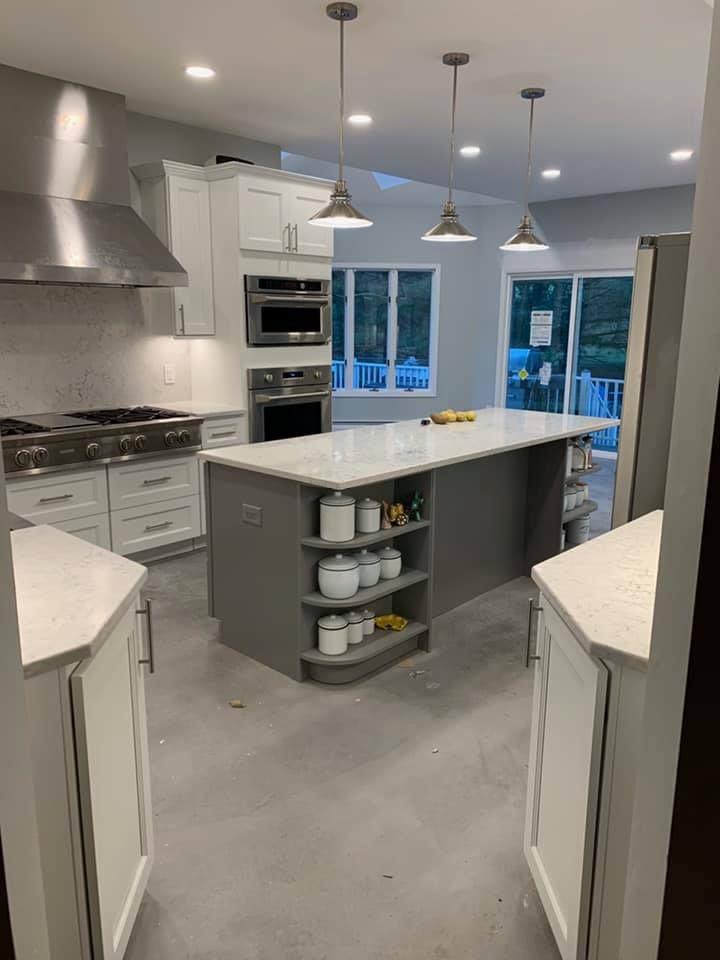 A kitchen with white cabinets , stainless steel appliances , and a large island.
