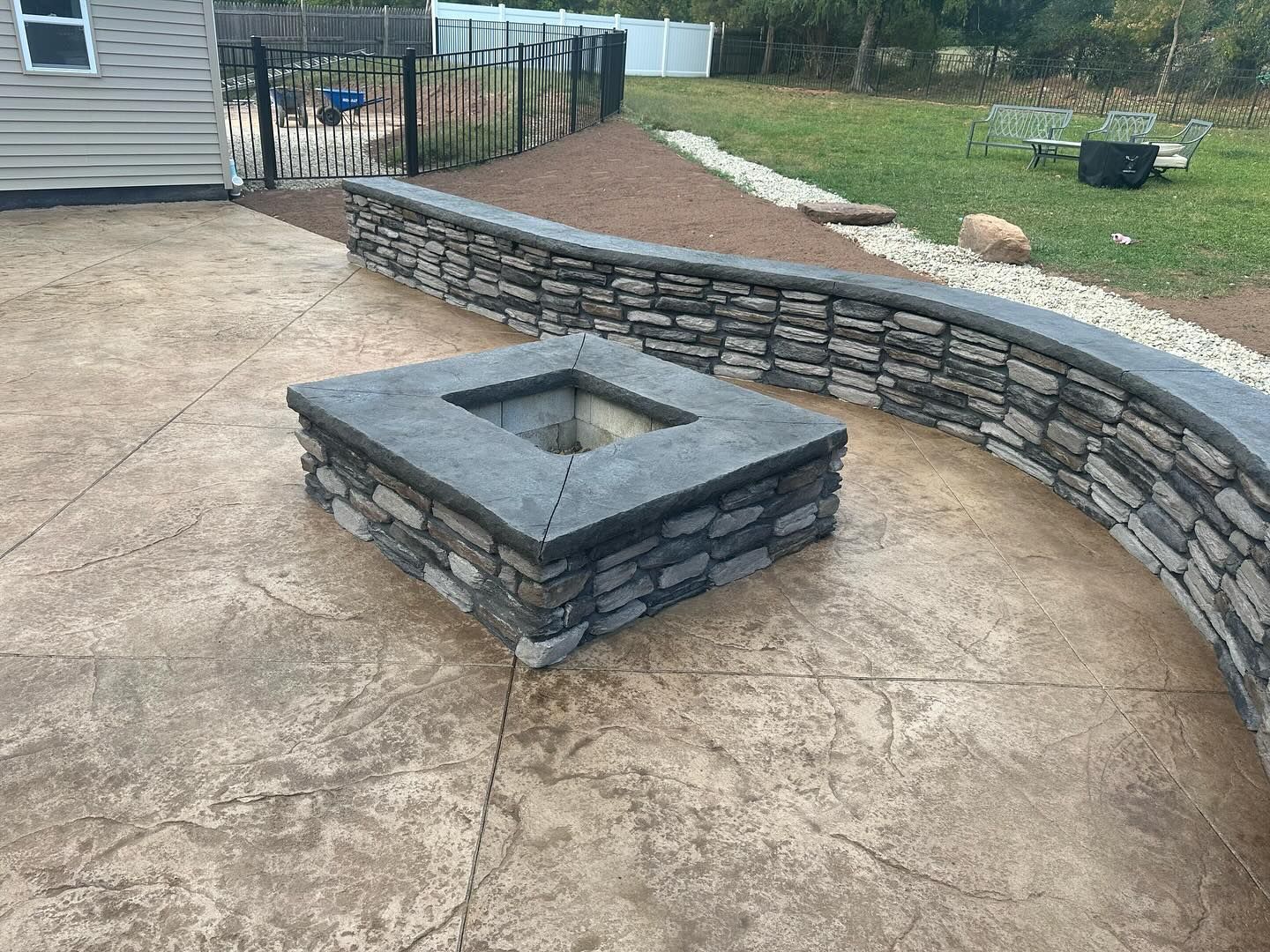 A fire pit is sitting on top of a concrete patio next to a stone wall.