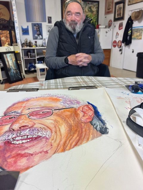 A man sits at a table with a painting of a man 's face on it