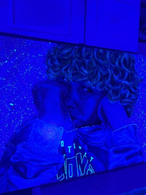 A painting of a person with curly hair is glowing in the dark.