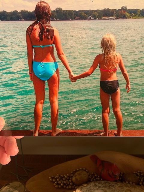 Two girls in bikinis are standing on a dock holding hands