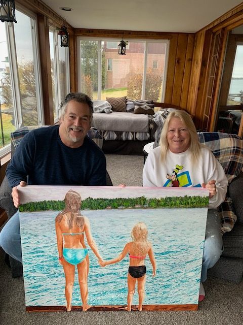 A man and woman are holding a painting of two women holding hands in the water.