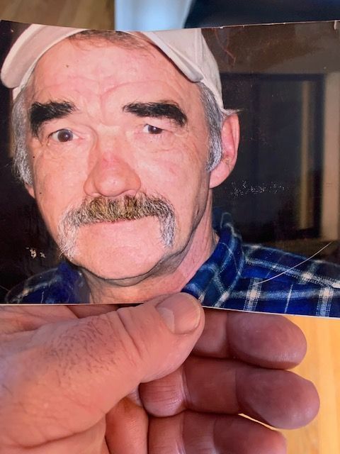 A man with a mustache is holding a picture of himself.