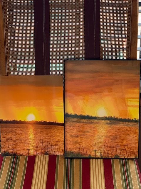 Three paintings of a sunset over a body of water are sitting on a striped rug.
