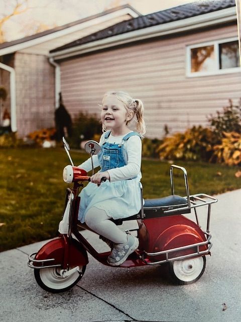 A little girl is riding a red toy scooter