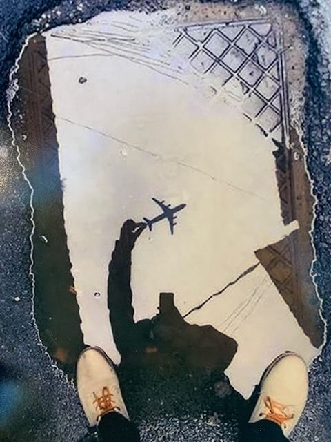 A person standing in a puddle with a reflection of an airplane