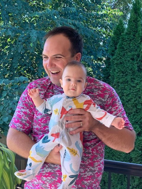 A man in a pink shirt is holding a baby in his arms.