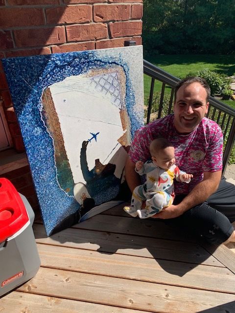 A man is holding a baby in front of a painting