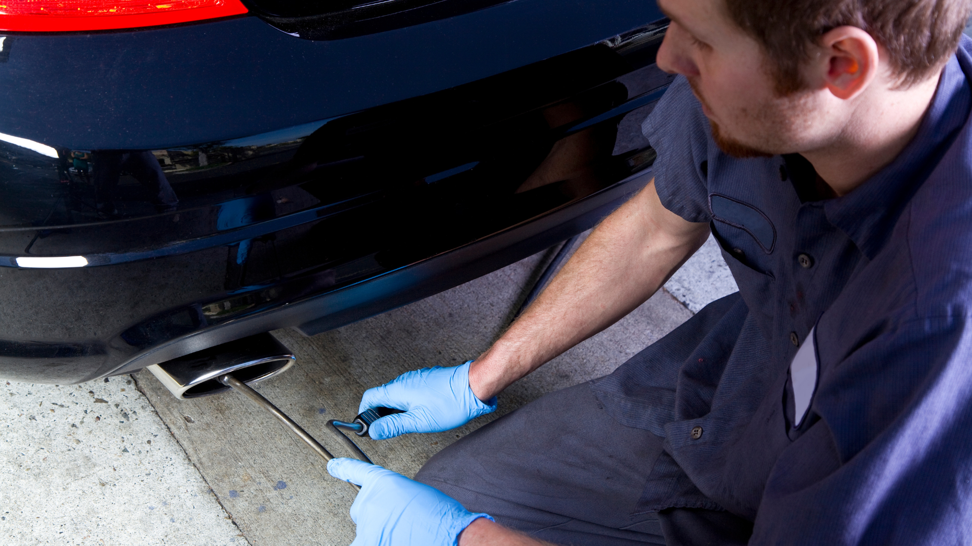A man wearing blue gloves is working on the exhaust pipe of a car.